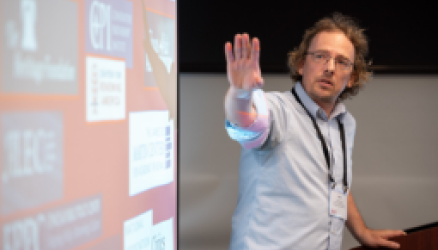 Presenter stands to the right of a screen with logos of conservative donors and holds his hand out toward the screen